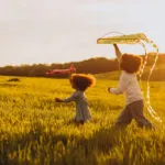 Crianças brincando com pipa e avião no campo ao entardecer (Créditos: Magnific)
