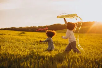 Crianças brincando com pipa e avião no campo ao entardecer (Créditos: Magnific)