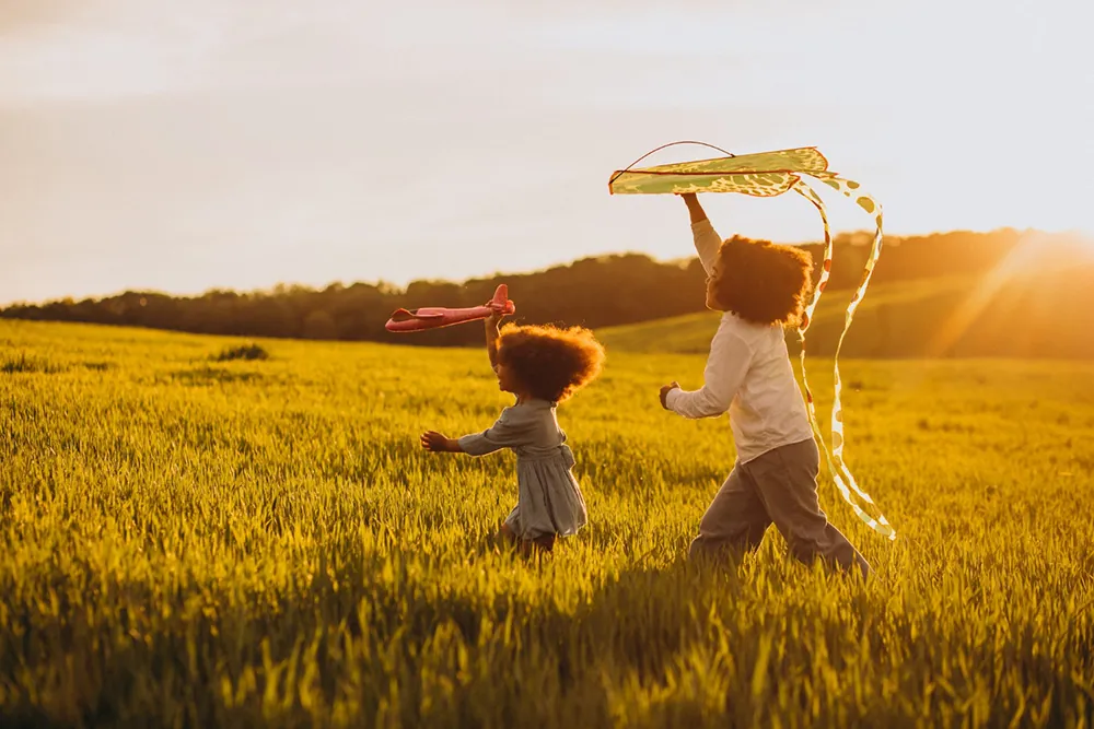Crianças brincando com pipa e avião no campo ao entardecer (Créditos: Magnific)