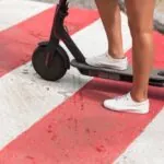 Pernas de pessoa em patinete elétrico sobre faixa de pedestres (Créditos: Magnific)