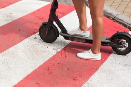 Pernas de pessoa em patinete elétrico sobre faixa de pedestres (Créditos: Magnific)