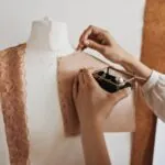 Mãos prendendo molde de costura em manequim com alfinetes (Créditos: Magnific/Freepik)